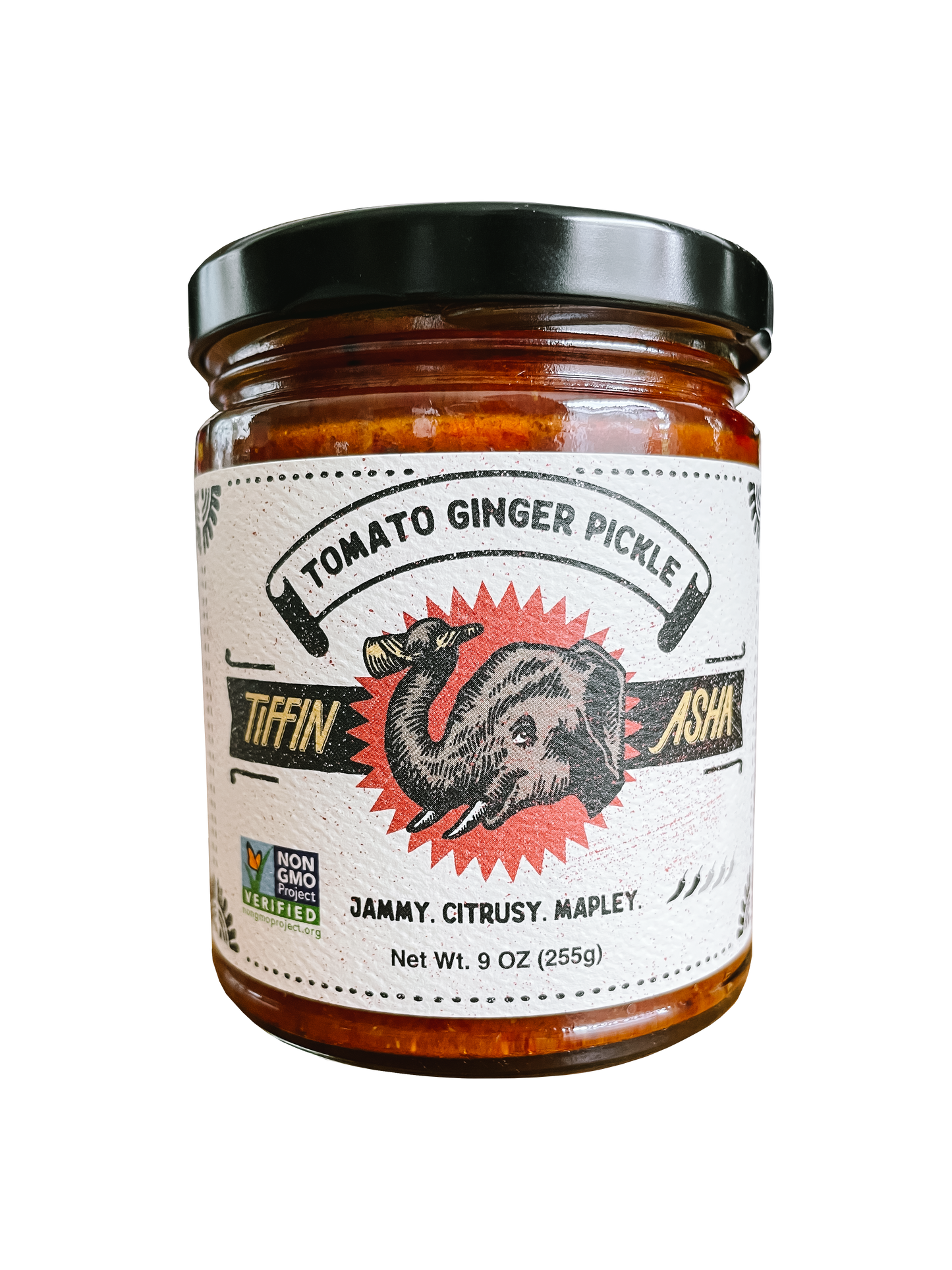 9 oz glass jar with black lid. Label reads: Tiffin Asha, with an elephant head and its trunk holding a dosa, Tomato Ginger Pickle, NON GMO project VERIFIED, tasting notes read: jammy, citrusy, mapley, shows 2 chili peppers for heat level.